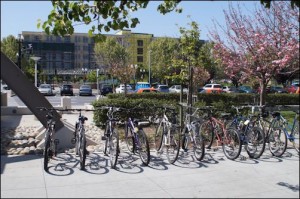 Yes, the Caltrain station provides bike racks -- and people are using them. But look carefully at this picture. Beyond the bikes the valuable land adjacent to the train station is consumed by surface parking lot.