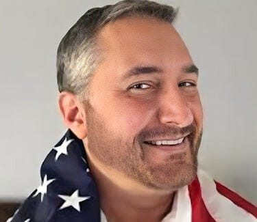 A man smiling while wrapped in an American flag, showcasing a confident and friendly demeanor.