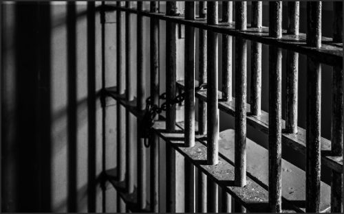Close-up of prison bars with shadows and a chain lock.