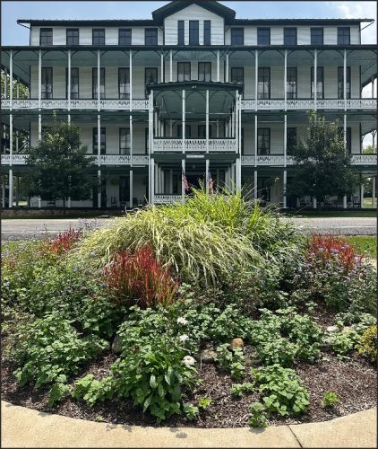 A historic building with multiple balconies, surrounded by a vibrant garden featuring various plants and flowers.