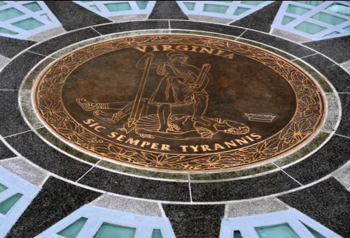 A close-up view of a circular seal for Virginia, featuring a figure holding a sword and a spear, surrounded by the phrase 'SIC SEMPER TYRANNIS' and decorative elements.