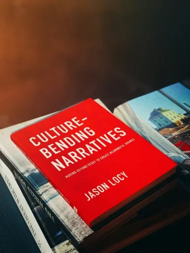 A close-up of the book cover titled 'Culture-Bending Narratives' by Jason Locy, displayed on a stack of books with a soft focus background.