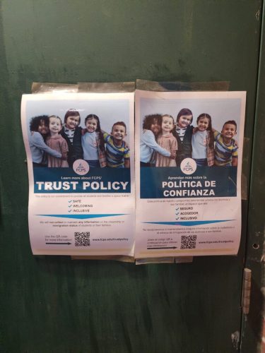 Two posters on a green door promoting Fairfax County Public Schools' Trust Policy, featuring diverse children together and highlighting safe, welcoming, and inclusive values.