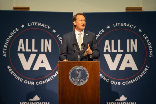 Governor Glenn Youngkin speaking at a podium with signs promoting literacy and education in Virginia.