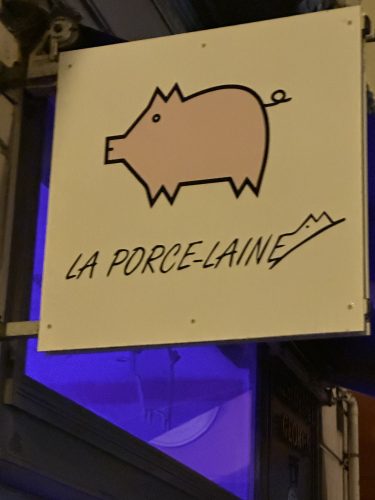 Sign for 'La Porce-Laine' featuring a stylized pink pig illustration, set against a dark background.