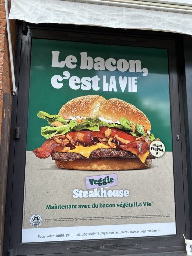 A poster showcasing a Veggie Steakhouse burger with plant-based bacon, lettuce, and cheese, featuring the text 'Le bacon, C'est LA VIE'.