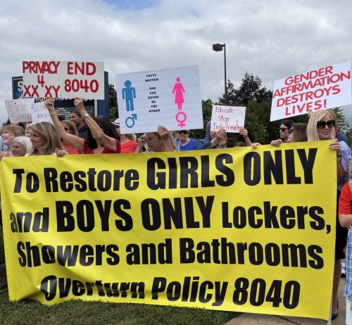A large group of people holding signs and banners at a protest, advocating to restore girls only and boys only locker rooms, showers, and bathrooms, while opposing Policy 8040.