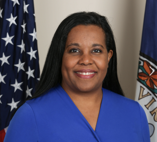 Portrait of Leader Charniele Herring, wearing a blue top, smiling at the camera with the Virginia state flag and an American flag in the background.