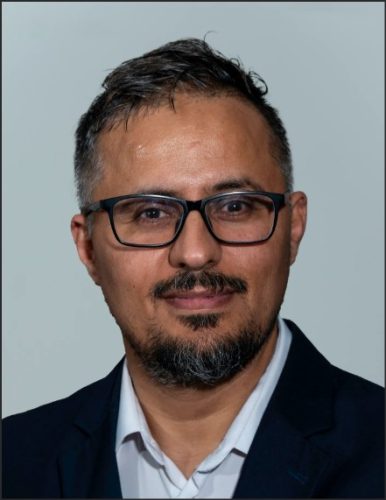 Portrait of Nasser Alsaadun, an Iraqi-American immigrant, wearing glasses and a dark suit, with a neutral background.