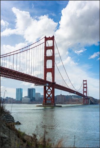 View of the Golden Gate Bridge spanning across a body of water, with blue skies and clouds in the background.