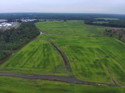 Aerial view of lush green farmland known as The Cove, bordered by a river and surrounded by trees, showcasing the historic agricultural land now protected by a conservation easement.