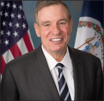 Portrait of a man in a suit smiling, with an American flag and a Virginia state flag in the background.