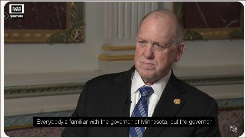 A man in a suit with a tie sitting in a formal setting, engaged in an interview.
