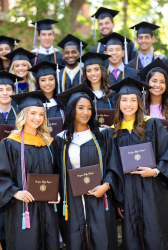 Group of high school graduates posing outdoors in caps and gowns, holding their diplomas.