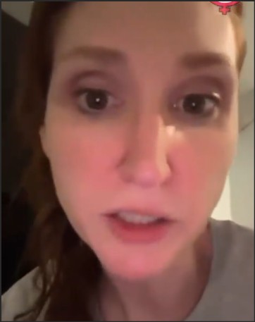 Close-up of a woman with long, reddish hair speaking directly to the camera in a casual indoor setting.