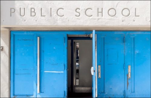 Exterior view of a public school entrance with blue double doors and the words 'PUBLIC SCHOOL' above.