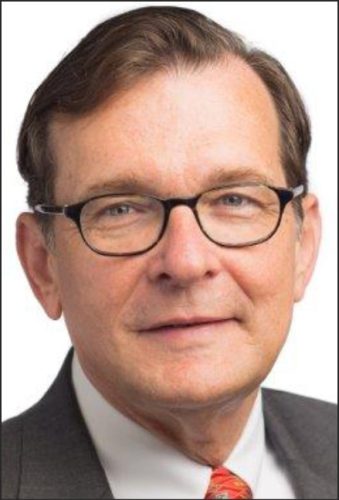 A middle-aged man with glasses and short brown hair, wearing a suit and tie, smiling at the camera.
