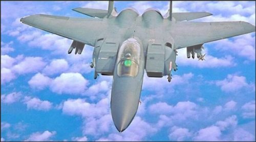 A military fighter jet flying above fluffy white clouds against a blue sky.