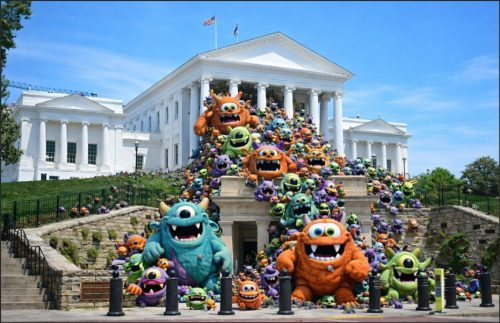 A large group of colorful, cartoonish monster plush toys piled in front of a white building with columns, resembling a government structure.