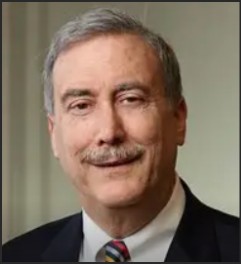 Close-up portrait of a professional man with gray hair and a mustache, wearing a dark suit and a striped tie, smiling softly.