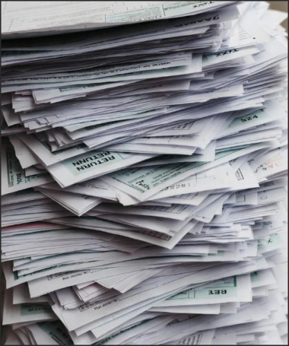 A large stack of paperwork, including forms and documents, organized in a messy pile.