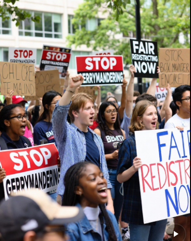 A diverse group of protesters holding signs that read 'Stop Gerrymandering' and 'Fair Redistricting Now' during a rally.