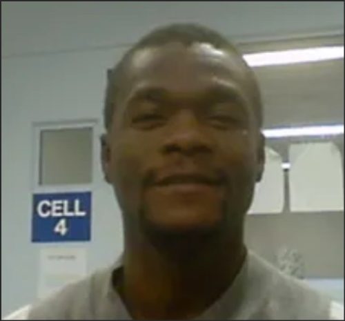 A man smiling in a hallway with a sign that reads 'CELL 4' in the background.
