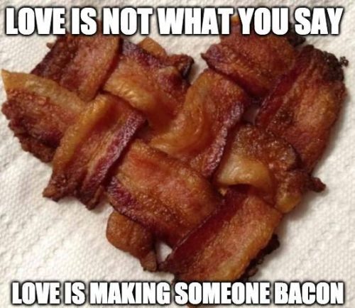 A heart shape made of woven strips of bacon with a humorous caption about love.