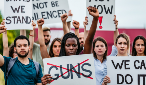 A diverse group of people participating in a protest, holding signs with messages against gun violence and advocating for action.
