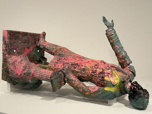A colorful contemporary sculpture of a figure lying down, partially supported by a metallic structure, featuring bold splashes of pink, green, and yellow.
