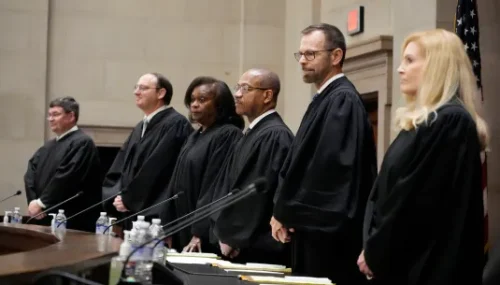 A lineup of five judges in black robes standing at a courtroom bench.