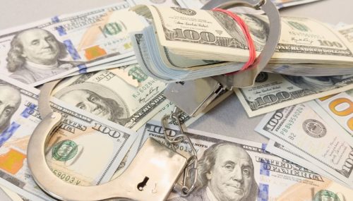 A pile of hundred dollar bills with a pair of handcuffs and cash secured inside.