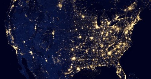 A satellite image of the United States at night, showcasing illuminated city lights against a dark background.