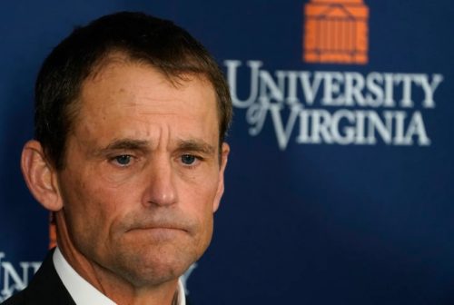 Close-up of a man with a serious expression, standing in front of a University of Virginia backdrop.