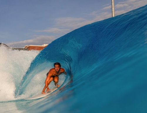 A surfer riding a wave, captured from inside the barrel of the wave, showcasing the vibrant blue water and a clear sky.